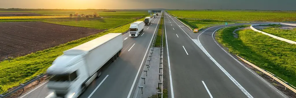 Many new modern trucks in a row driving towards the sun at idyllic sunny day. Fast blurred motion drive on the freeway. Freight scene on the motorway near Belgrade, Serbia.