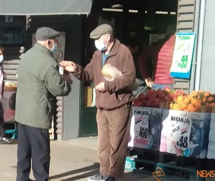 Dos personas mayores charlan frente a una frutería de Zamora