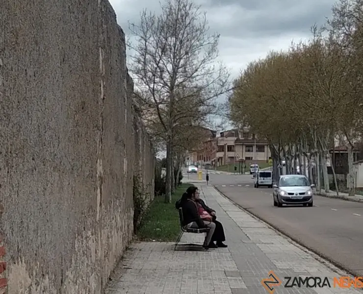 Dos personas conversan sentadas en un banco de Pinilla