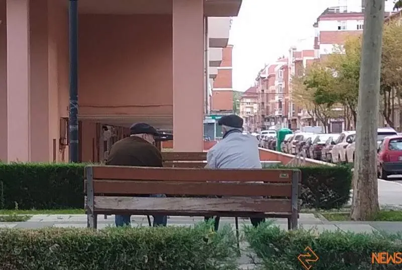 Dos personas mayores conversan sentados en un banco de Zamora