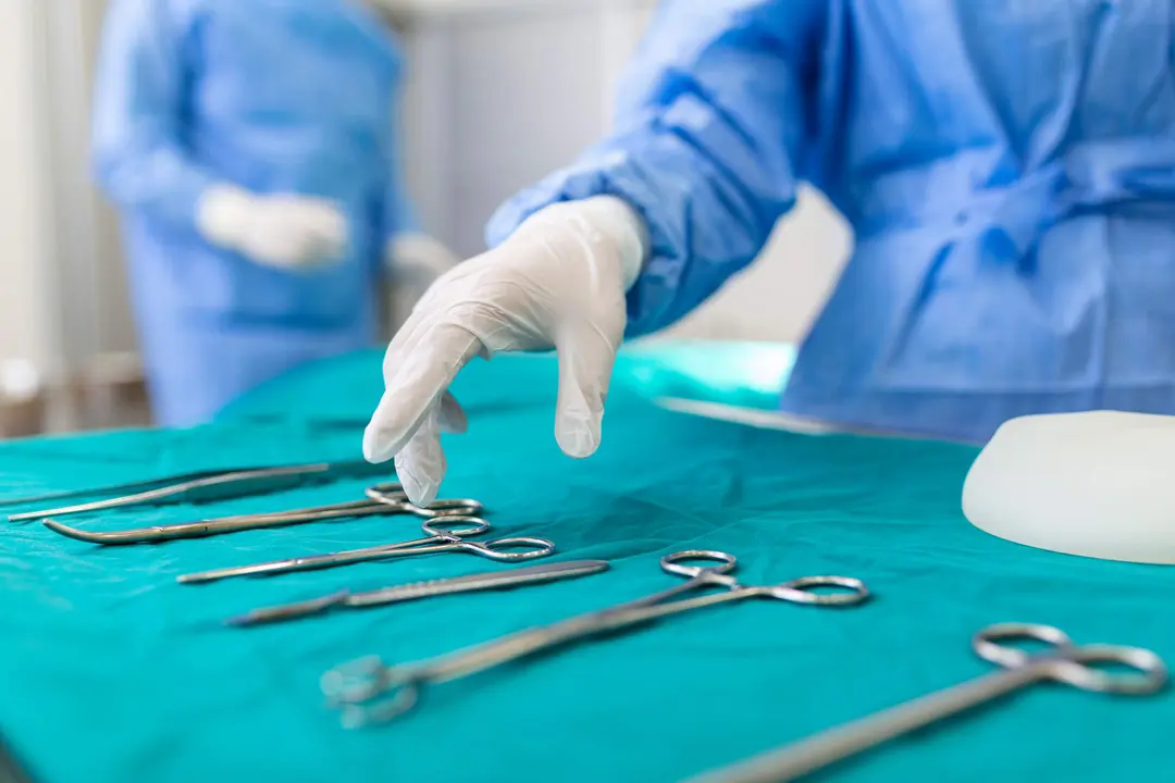 Nurse hand taking surgical instrument for group of surgeons at background operating patient in surgical theatre. Steel medical instruments ready to be used. Surgery and emergency concept