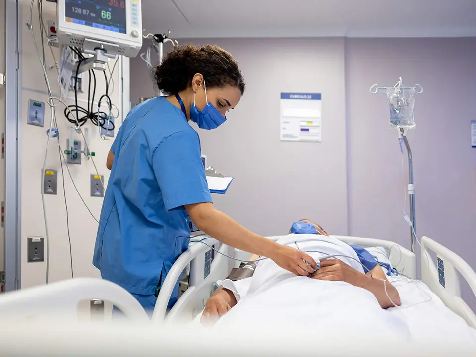 Latin American nurse checking on a patient lying in bed at the hospital - Intensive Care Unit concepts
