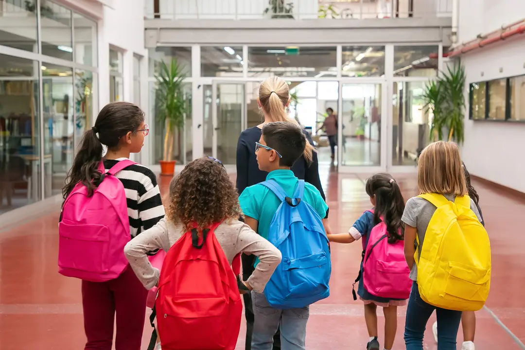 Group of children with female teacher walking in school corridor. Back view. Education or back to school concept