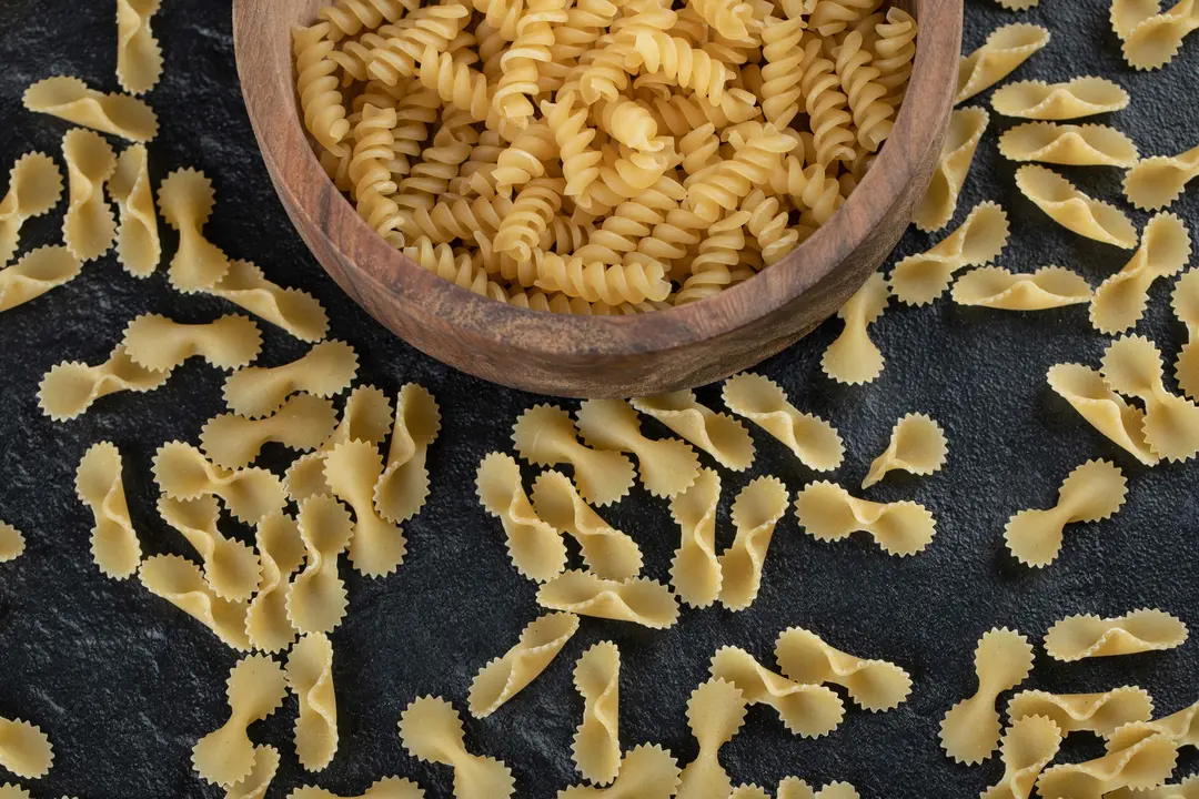 A wooden bowl full of raw girandole pasta . High quality photo