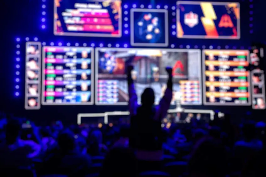 Blurred background of an esports event - Fan on a tribune at tournaments arena with hands raised.