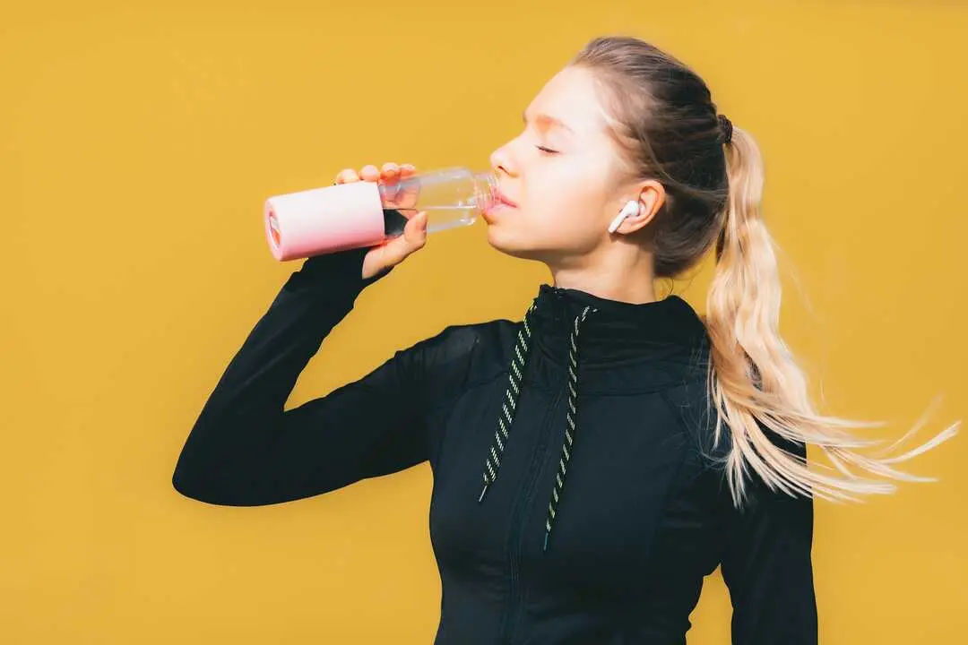 Attractive caucasian girl on yellow isolated background with wireless headphones in sport suit make workout, run and drinking water