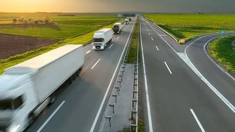 Many new modern trucks in a row driving towards the sun at idyllic sunny day. Fast blurred motion drive on the freeway. Freight scene on the motorway near Belgrade, Serbia.