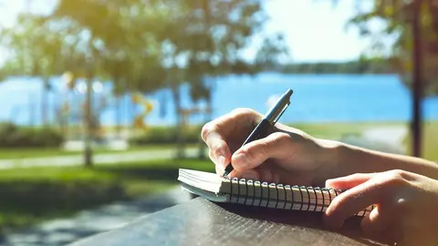 girls hands with pen writing on notebook in park