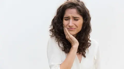 Frustrated unhappy woman suffering from toothache. Wavy haired young woman in casual shirt standing isolated over white background. Dental problem concept