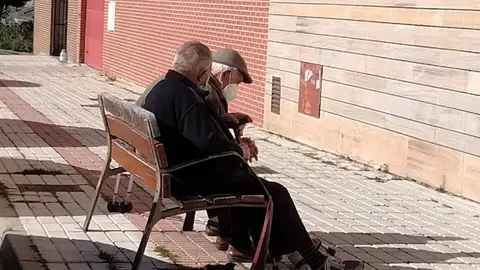 Dos hombres mayores charlan en un banco de la ciudad
