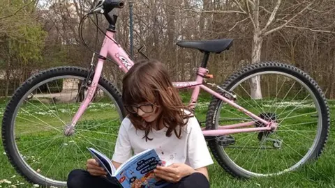 Niña leyendo un libro junto a su bici. Foto AAVV Valorio-San Lázaro