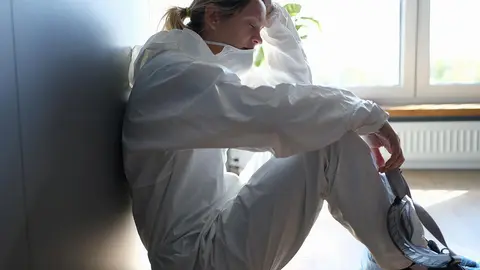 Tired female doctor in medical protective suit and mask in hands after work in clinic. Harsh working conditions of doctors in coronavirus pandemic concept