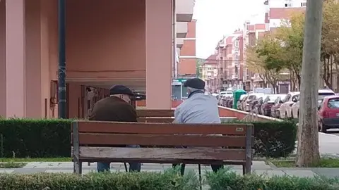 Dos personas mayores conversan sentados en un banco de Zamora