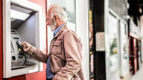 Pensionista sacando dinero de un cajero. Fotografía de archivo