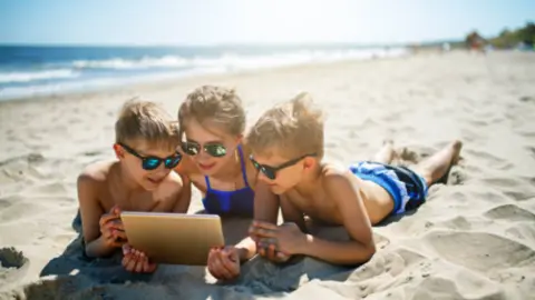 Niños utilizando una tableta en l aplaya. Fotografía de archivo