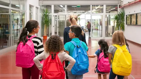 Group of children with female teacher walking in school corridor. Back view. Education or back to school concept