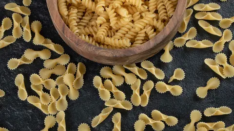 A wooden bowl full of raw girandole pasta . High quality photo