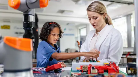 Female teacher helping young schoolboy to build robot kit in after-school robotics club. Children learning robotics in Elementary school. Science for kids. STEM.