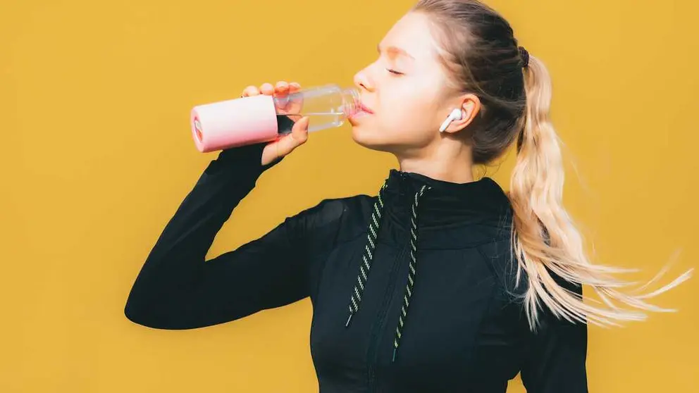 Attractive caucasian girl on yellow isolated background with wireless headphones in sport suit make workout, run and drinking water